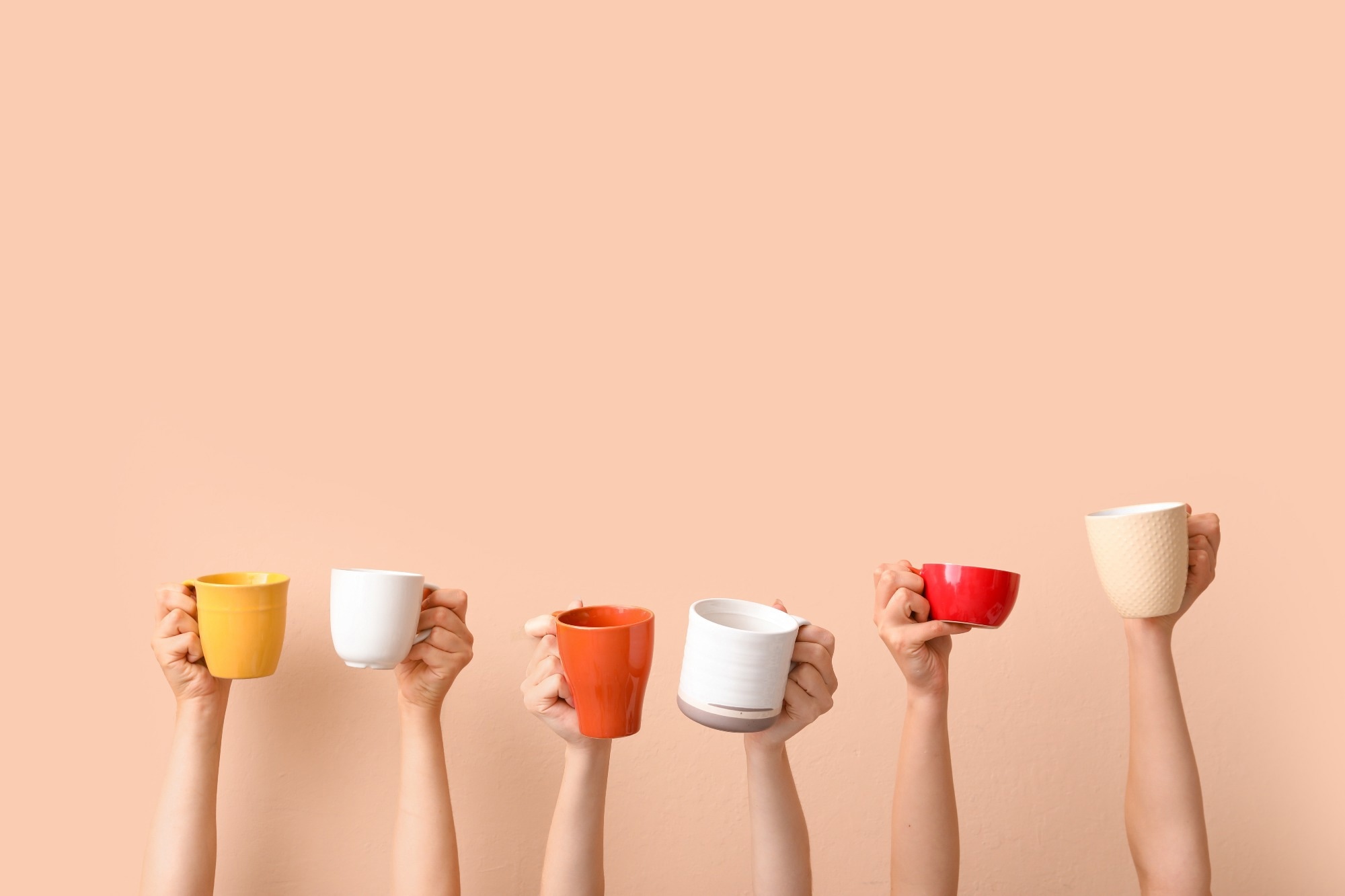 Women holding cups of hot coffee on beige background.