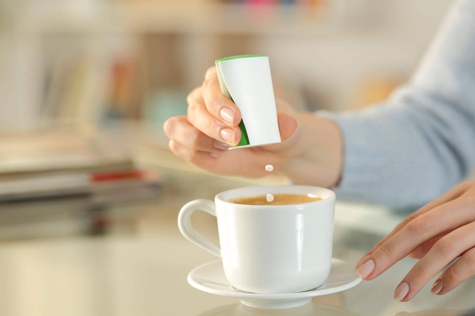 Close up of woman hand throwing sweetner pills on coffee cup on a desk at home