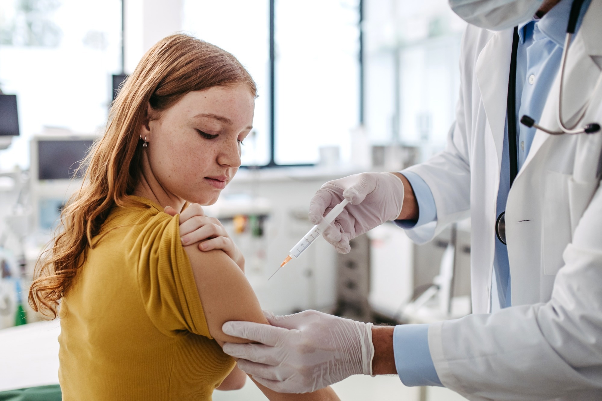 pediatrician injecting vaccine into teenage girl arm