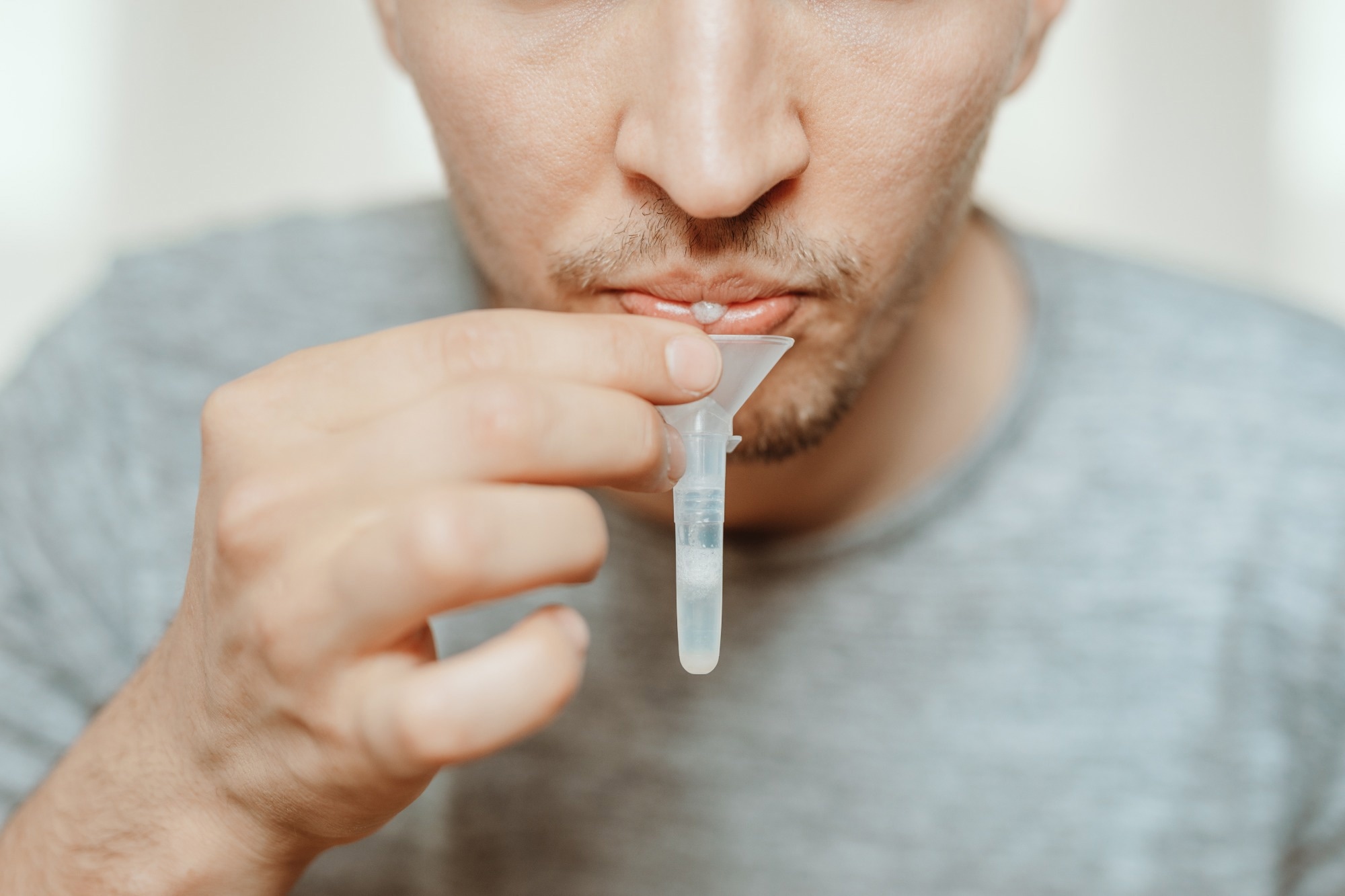 man spitting with mouth through funnel in plastic tube to collect sample