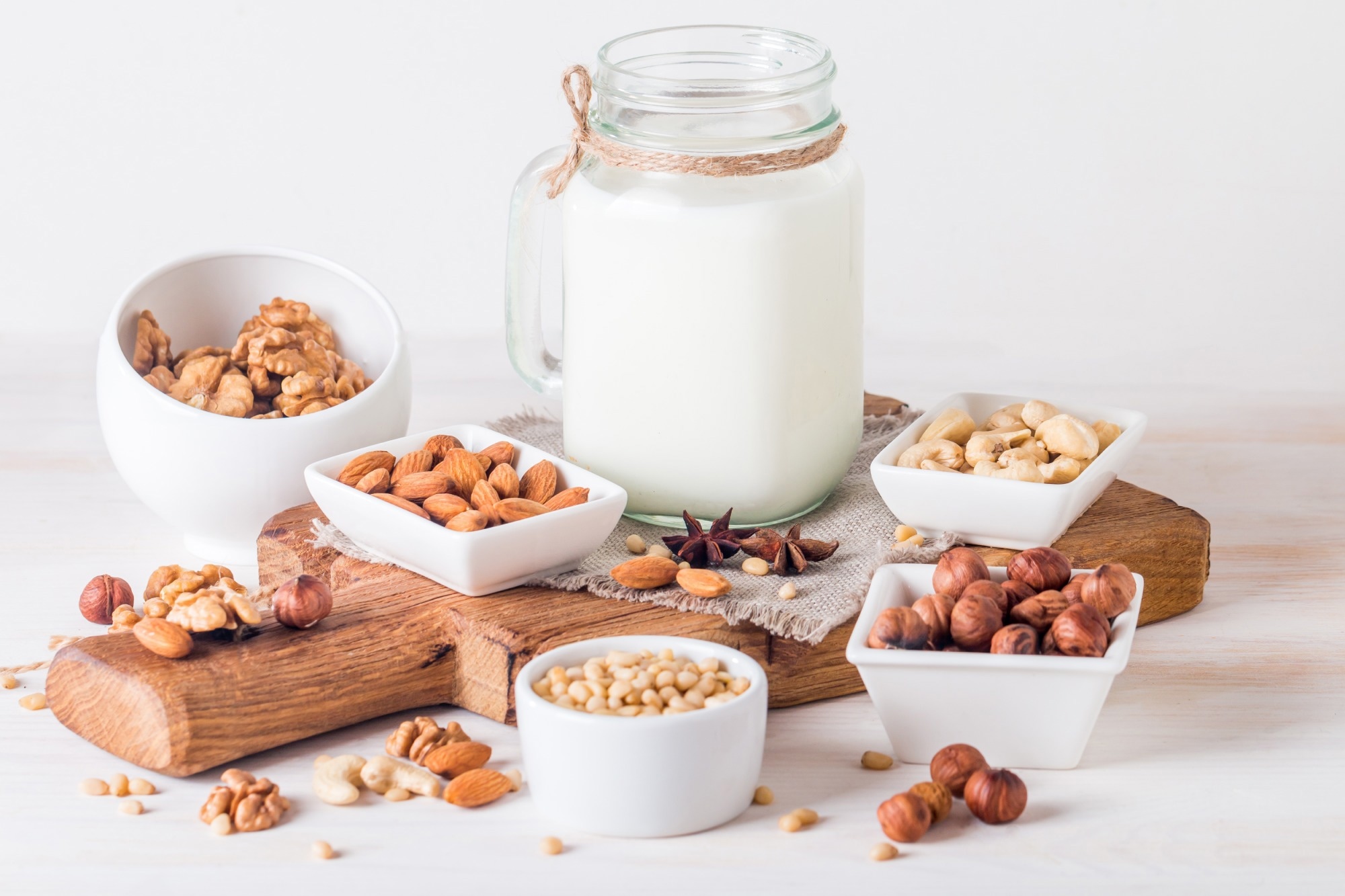 Vegan milk from nuts in glass jar with various nuts on white wooden background