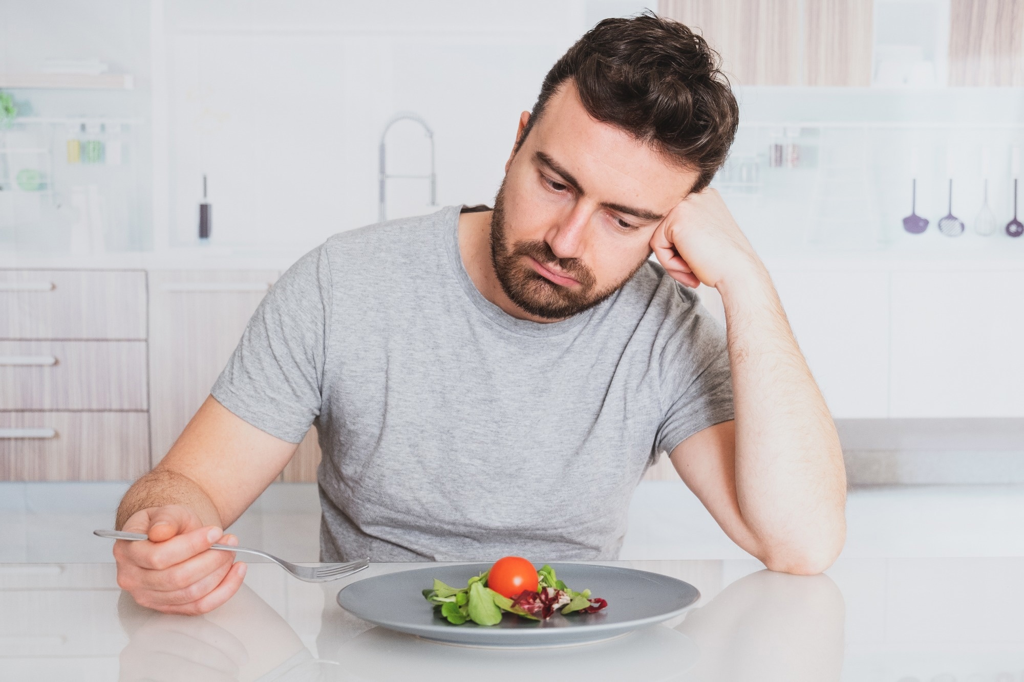 Man looking depressed and stressed with a plate of vegetable and a fork in his hands