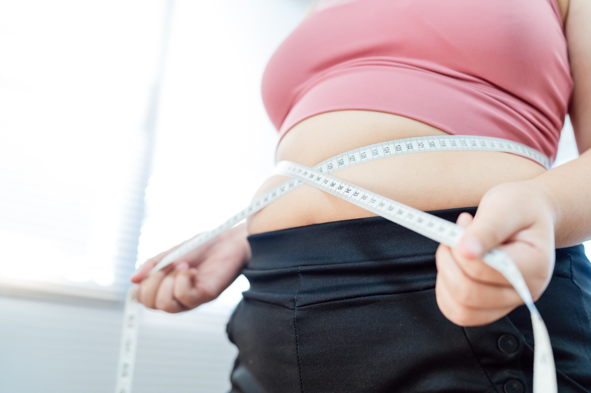 Overweight woman in pink sports top pulling measuring tape around waist