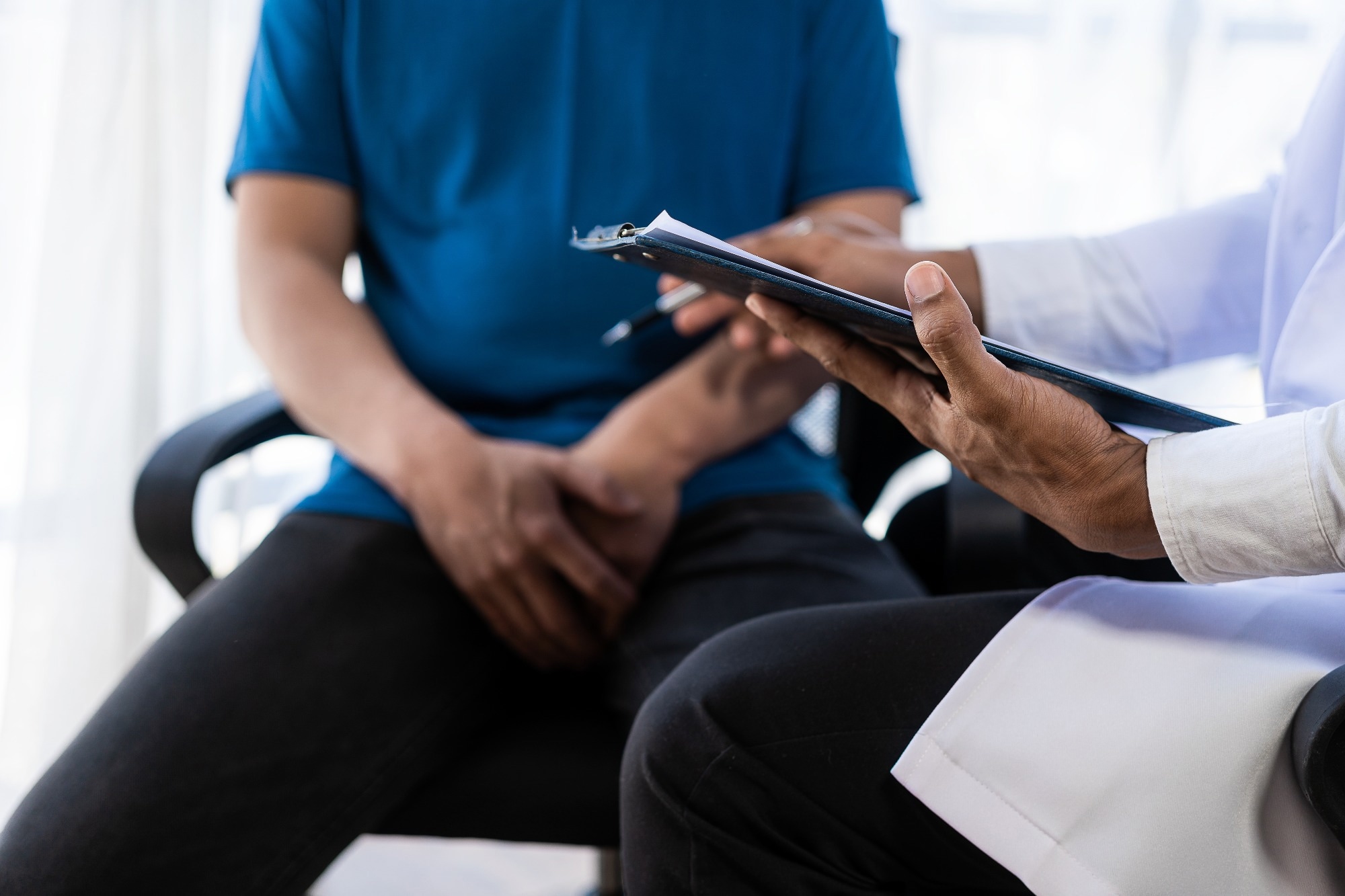 Male patient sitting in doctors office. Man hands holding crotch area